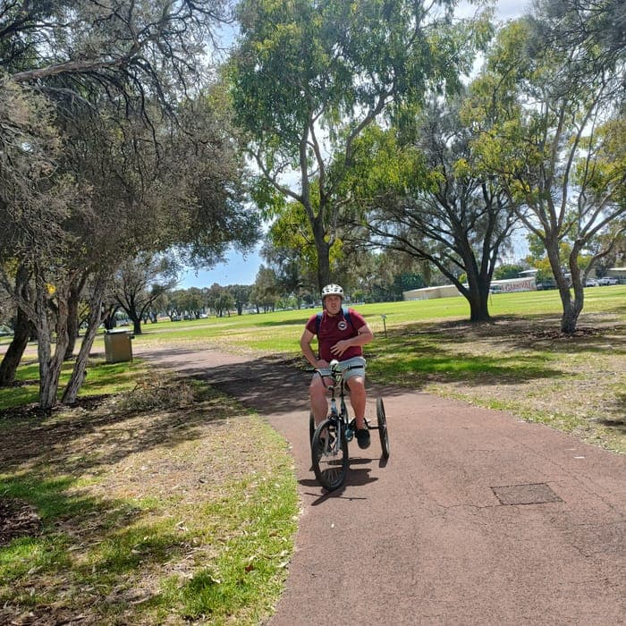 A participant riding an adaptive tricycle through a Perth park