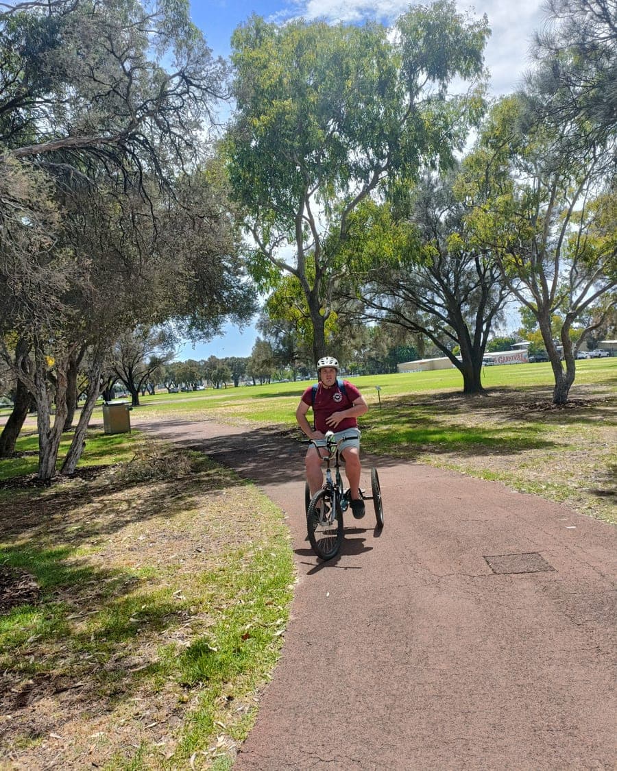 A participant riding an adaptive tricycle through a Perth park